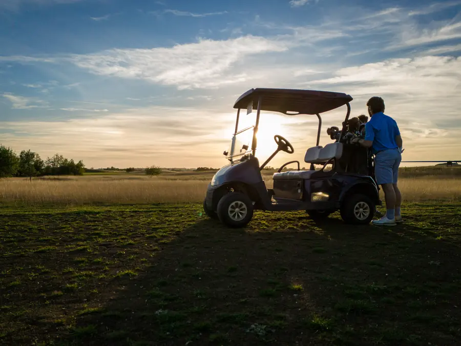 Two golfers by a buggy against the low sun