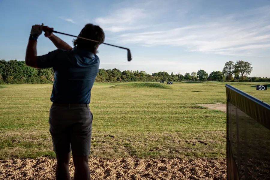 A golfer at the top of the swing on the range tee line, evening