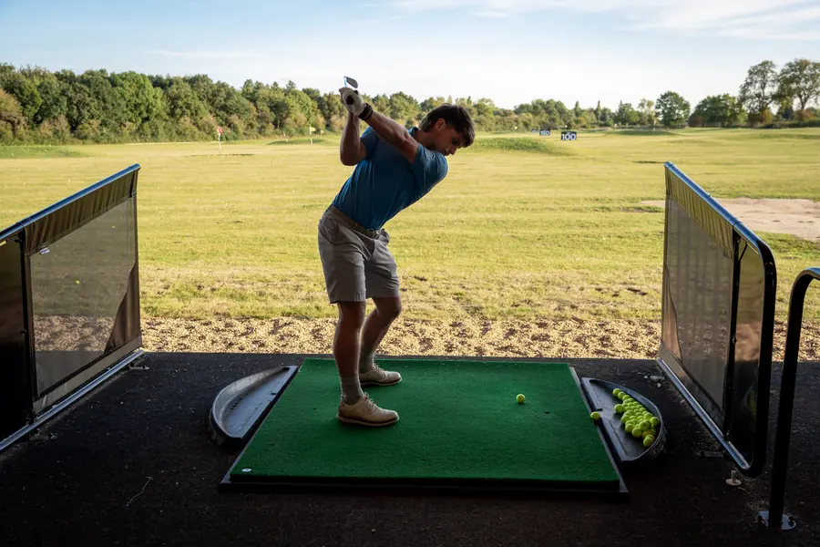 A golfer at the top of the backswing on a range mat, the range beyond