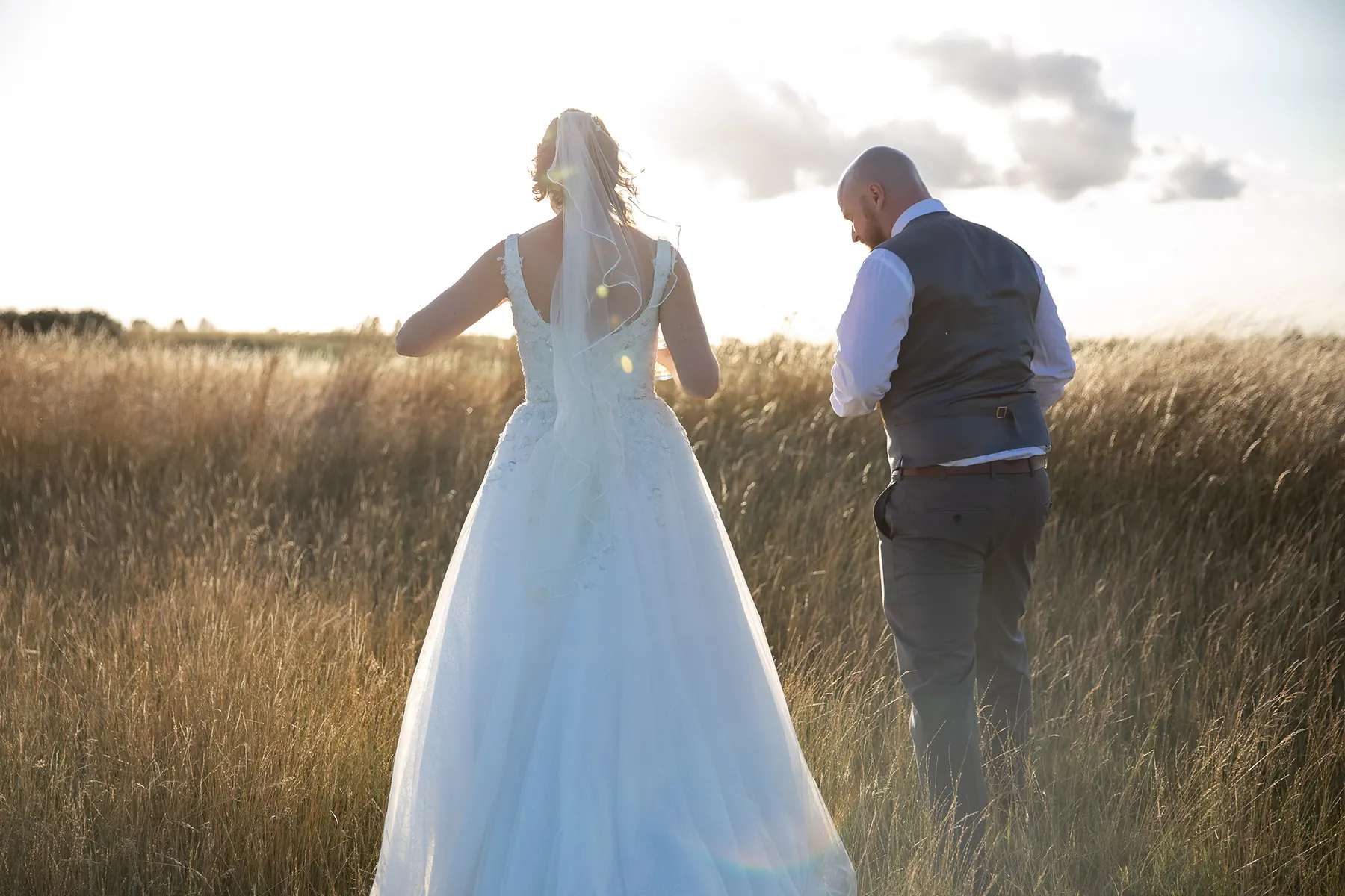 A bride and groom walking into the long grass, from behind