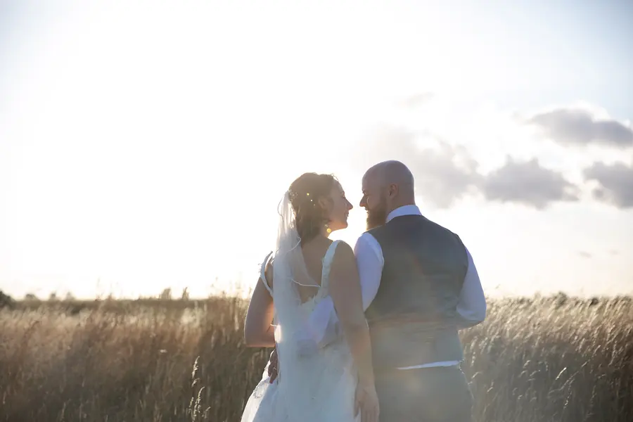 A bride and groom in the grasses against the evening sky